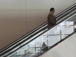  WS Businessman riding up escalator, with reflection in glass side of escalator of businessmen meeting and shaking hands / Seattle, Washington, United States Stock Footage