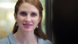 Assertive businesswoman speaks out in conference-room meeting, office workers cross in background Stock Footage