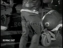 1942: GROUND CREW: Bombs under airplane, one hanging on cable, crewman standing behind. US Ground Crew male moving single bomb on bomb carriage, hand truck. TU MS Bomb being hoisted into bomb bay. WS Bomb Bay doors under airplane closing. WWII Instructional Video