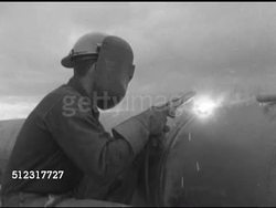 1952: ARC WELDING: LA MS (BESIDE) Man in welding helmet holding stick welder, putting helmet down, welding pipe edges, replacing consumable electrode on stick. Manual metal arc welding, stick welding, field work. Instructional Video