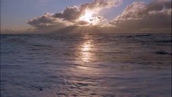 Waves wash up onto a beach and reflect the glowing sun. Stock Footage