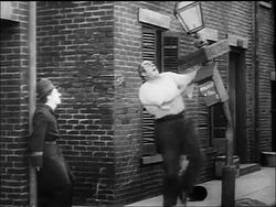 B/W 1917 large man (Eric Campbell) proving strength to cop Charlie Chaplin by bending street lamp Stock Footage