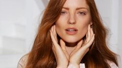 Close-up of red head touching her face and neck while hair blows in breeze with a smile Stock Footage