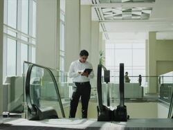 Businessman using digital tablet and ascending on escalator then tripping in office lobby / Provo, Utah, United States,  Stock Footage