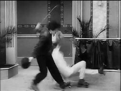 B/W 1916 Charlie Chaplin as Little Tramp roller skating + knocking over other men Stock Footage
