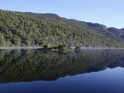 Mist rolls across forested mountain lake at dawn Stock Footage