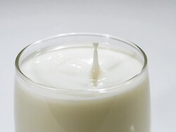 Drop of Milk falling into Glass against white background, slow motion Stock Footage