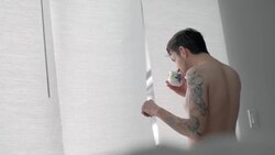 Young man stands with morning coffee and stares out hotel window Stock Footage