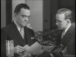 A man talks to J. Edgar Hoover as they look at documents. News Clip