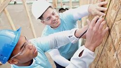 Men measure and mark plywood for house being built for charity Stock Footage