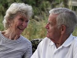 Dolly shot of affectionate elderly couple talking while sitting on a couch outdoors in slow motion Stock Footage