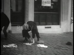 1936: BELGIUM: REXISM PROPAGANDA: MS Man putting up anti-Degrelle poster 'Degrelle serves Hitler.' WS Two men attack Rexist newsman on street. HA WS Rexist newsmen handing out papers. VS Rex newspaper headlines, men reading papers. Nazi, Brussels Instructional Video