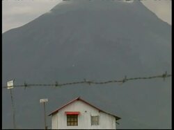 MS wooden house, tilt up slope of volcano in background to a column of grey smoke and ash cloud billowing from crater, Mount Tunguragua, Ecuador Stock Footage