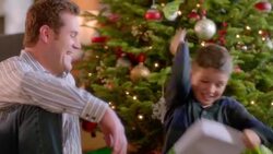 Mom and dad laugh as boy tears into wrapping paper under Christmas tree (dolly-shot) Stock Footage
