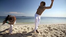 Opponent ducks as capoeira fighter kicks over his head on scenic Ipanema Beach Stock Footage