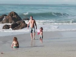 MS TS Boy, girl and man play with balloon and water balloon on beach with wavebreak  then boy walks toward squirting water in his mouth from water balloon / Montezuma, Puntarenas, Costa Rica Stock Footage