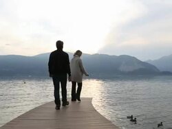 Couple walk onto lake pier, look off to sunrise Stock Footage