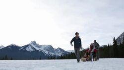 Young couples sledding in snowy field below mountains Stock Footage
