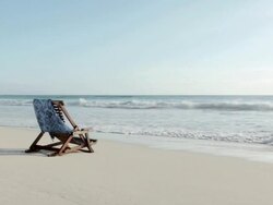 Deck chair on sandy beach at water's edge Stock Footage