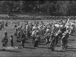 1927: POLITICS: HA WS Sioux Nation Native American peoples in traditional clothing dancing in field lined w/ cars, MS Dancing in celebration, WS U.S. President Calvin Coolidge wearing chief headdress sitting in stands  (Sioux name: Chief Leading Eagle Instructional Video