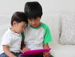 Two children playing with a tablet together on the sofa at home Stock Footage