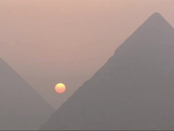 Long Shot, static  - An orange sun glows through the smog between the Great Pyramids of Giza / Egypt Stock Footage