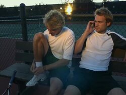 MS, Two young men sitting on bench at tennis court, one talking on mobile phone, Santa Barbara, California, USA Stock Footage