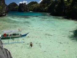 High angle caucasian woman in bikini wading towards outrigger boat floating in idyllic tropical inlet / Small Lagoon, Miniloc Island, Bacuit Archipelago, El Nido, Palawan, Philippines Stock Footage