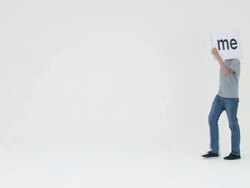 Man walking and covering face with sign that reads me, he stops and shows his face Stock Footage