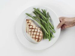 CU Woman hand entering setting down round white plate with grilled chicken breast and asparagus / Omaha, Nebraska, United States Stock Footage