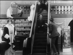 B/W 1916 Charlie Chaplin being chased down the "up" escalator by large man (Eric Campbell) Stock Footage
