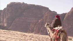 Arab people in traditional clothing ride camels through a desert in Wadi Rum, Jordan. Stock Footage