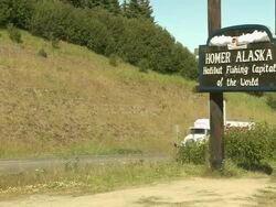 "Wooden sign reading ""Homer. Alaska.  Halibut fishing capital of the world."" at side of Sterling Highway, visible with traffic passing both ways, upon entrance to Homer, Kenai Peninsula, Alaska." Stock Footage