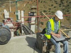 HA young engineer sitting in construction site, working on laptop computer, at end of clip looking to camera Stock Footage