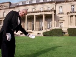 Wide shot butler on lawn smiling at CAM and extending arm toward mansion in welcoming gesture Stock Footage