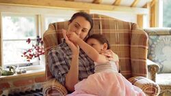 Mother and daughter cuddling and touching hands in armchair Stock Footage