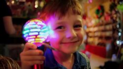 Young boy holds up spinning light to camera smiling in novelty shop Stock Footage