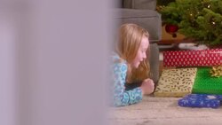 Cute young girl crawls cautiously up to Christmas tree to inspect presents (dolly-shot) Stock Footage