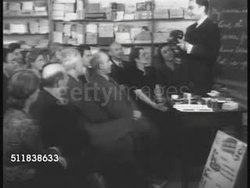 1941: AMERICANIZATION CLASS: Instructor at blackboard w/ adult immigrants. ESL CLASS: Instructor working w/ adult class, SOT 'This is a telephone...answering...what do I say?' Male in class saying, 'Good-bye, Please.' Group correcting him, 'Hello' Instructional Video