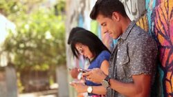Brazilian friends lean against graffitied wall and text on smartphones Stock Footage