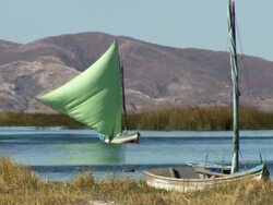 Boat with bright green sail on Lake Titicaca, with reeds and mountains in b/g, another boat in f/g, near Tiwanaku Tiahuanaco/Tiahuanacu, Bolivia Stock Footage