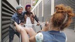 Cool young friends taking photograph with camera phone at shopping cart in urban alley Stock Footage