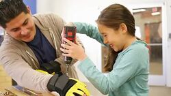 Instructor at woodworking workshop day camp for children teaches girl about using a drill Stock Footage