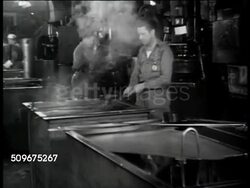1943: WWII INDUSTRY: Men working at furnaces, male cooling airplane part in water trough. Male worker taking heated ring out of furnace, metal cooling in water, steam rising. Instructional Video