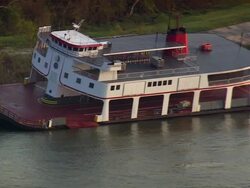 Aerial zoom in ferry boat half-submerged on bank of Mississippi River / trees and houses in background Stock Footage