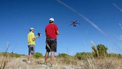 Two UAV pilots controlling drone takeoff on sunny hilltop Stock Footage