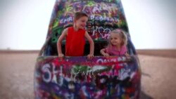 Young boy and young girl jump up and down while peeking out of a graffiti painted Cadillac sticking out of the ground at Cadillac Ranch Stock Footage