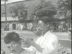 1950: KOREAN WAR: SEOUL: VS Korean barber cutting hair of another Korean male on war torn street. VS People listening to government official speaking outside building (no SOT). Korea Instructional Video