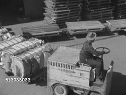 1952: NEW ORLEANS PORT: HA TD TRACKING Male worker driving line of connected railroad carts loaded w/ bales of cotton out of warehouse & up to dock.     Shipping, moving, industry, commercial, cargo. Instructional Video