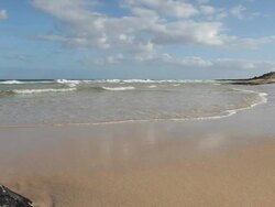 Gentle surf walks across beach, road above Stock Footage